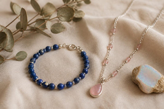 Brățară din lapis lazuli și colier cu cuarț roz, lângă o bucată de opal, pe in crem